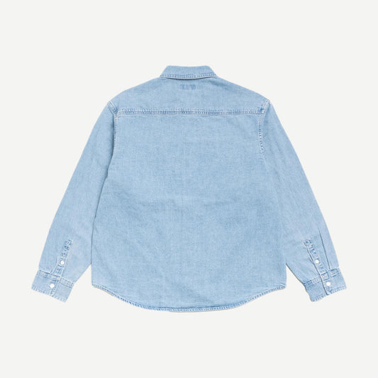 Light denim work shirt by Stussy, featuring long sleeves, collar, and button closure, styled as a casual denim shirt.