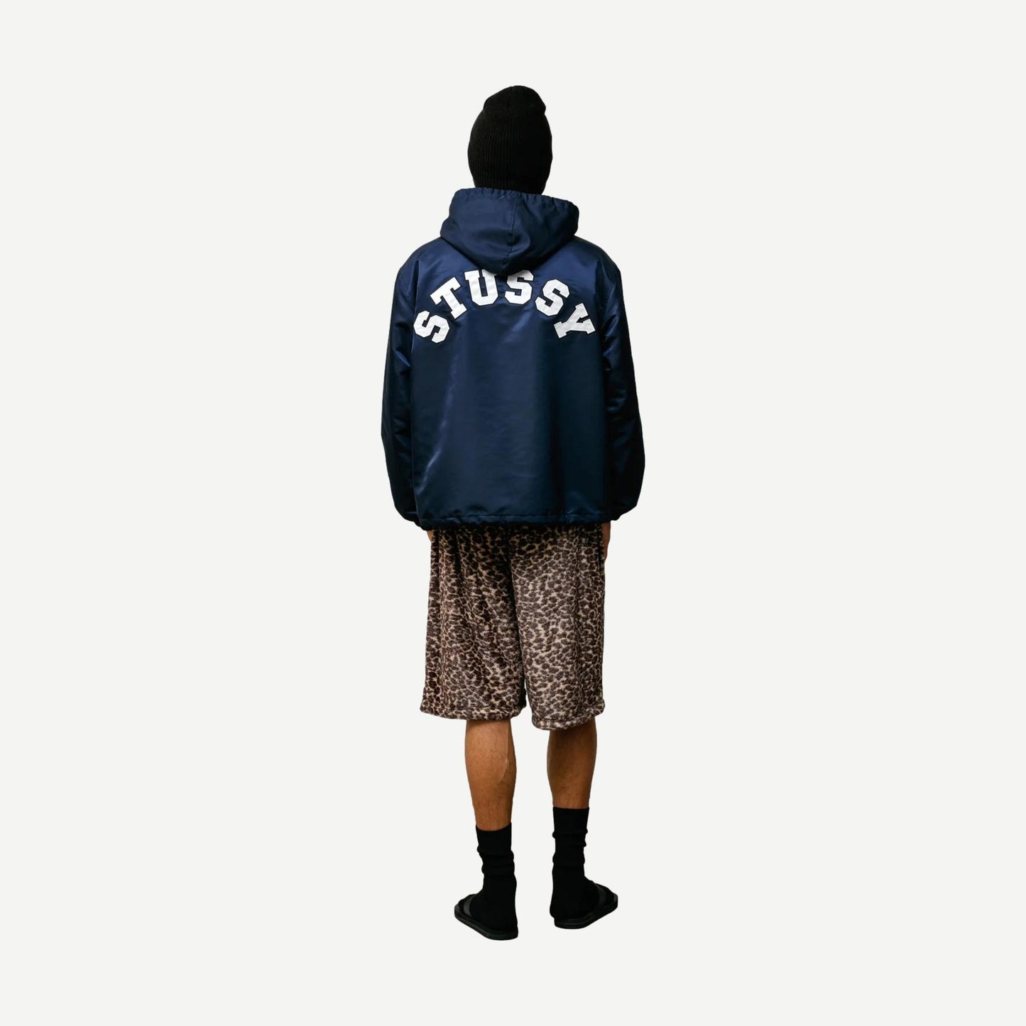 Navy hooded Stussy coaches jacket with front pockets and drawstring hood, displayed on a hanger.