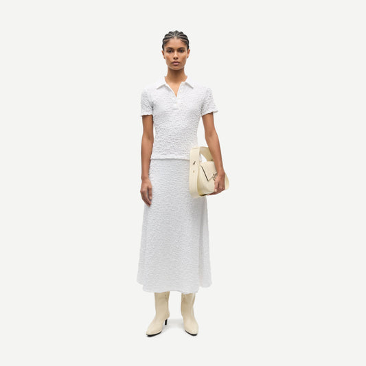 White Sadaisy SS Polo shirt by Samsoe Samsoe, shown on a hanger with a close-up of the fabric and collar detail.