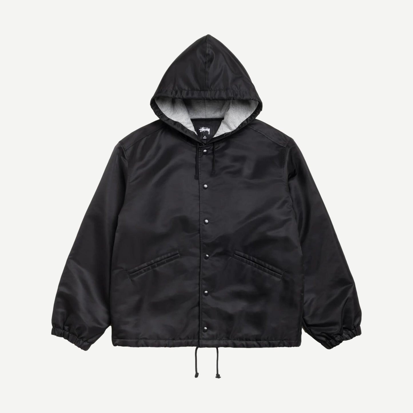 Black Stussy hooded coaches jacket with front pockets and drawstring hood, displayed on a hanger.