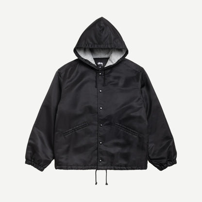 Black Stussy hooded coaches jacket with front pockets and drawstring hood, displayed on a hanger.