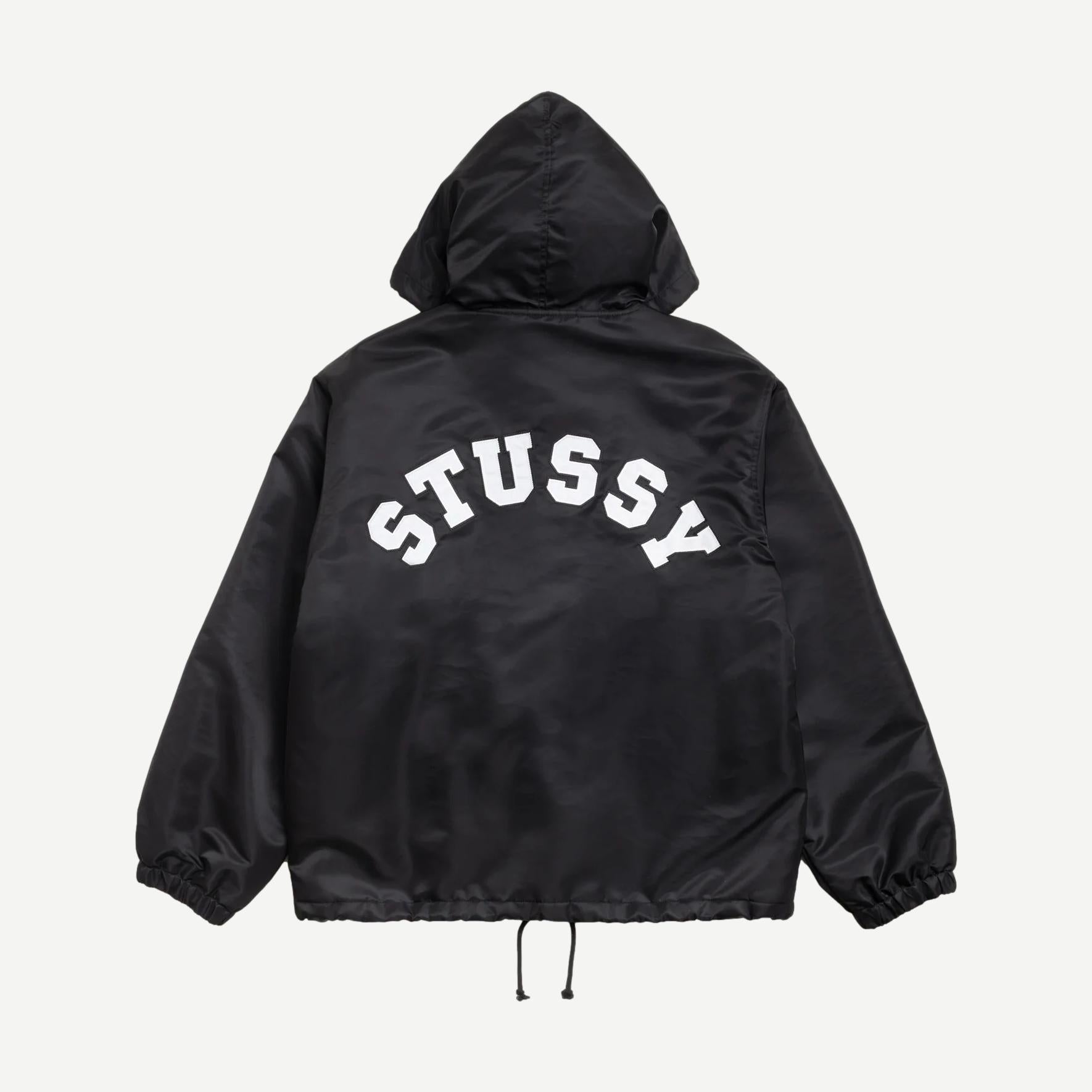 Black Stussy hooded coaches jacket displayed on a hanger, showcasing its casual style and front zipper design.