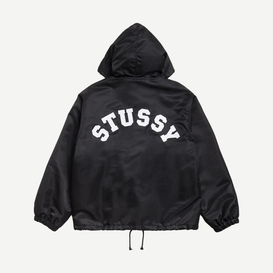 Black Stussy hooded coaches jacket displayed on a hanger, showcasing its casual style and front zipper design.