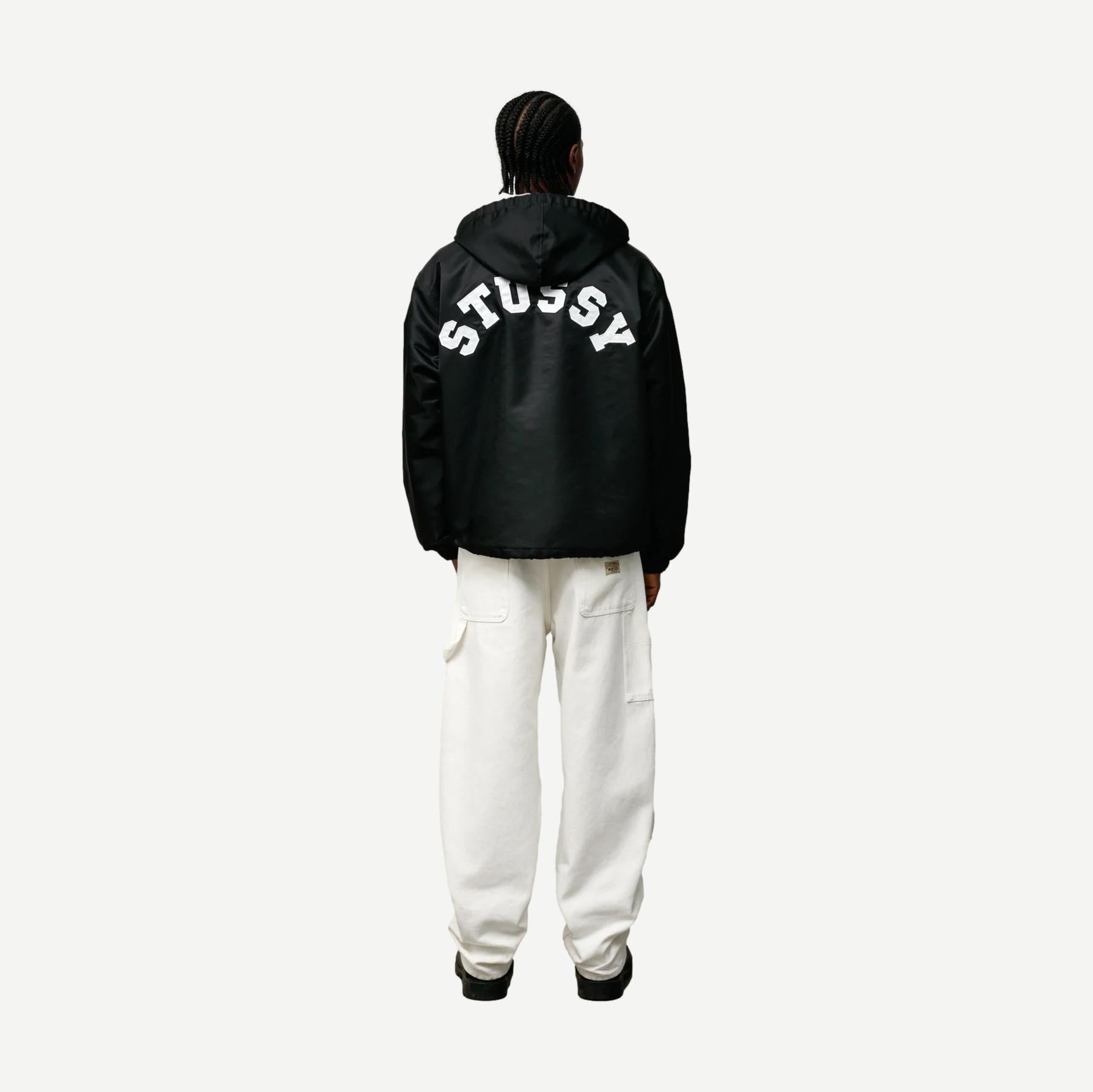 Black Stussy hooded coaches jacket with front pockets and adjustable drawstrings, displayed flat on a white background.