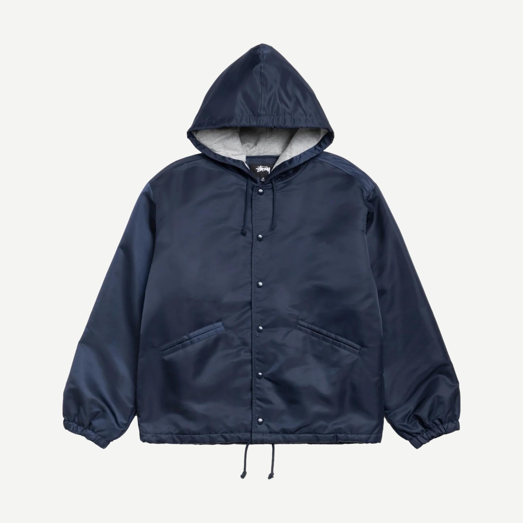 Navy Stussy hooded coaches jacket with front pockets and adjustable drawstrings, displayed on a hanger.