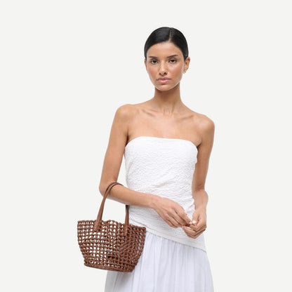 Staud Caro Bucket Bag in tan leather with adjustable shoulder strap and minimalist design, shown on a neutral background.