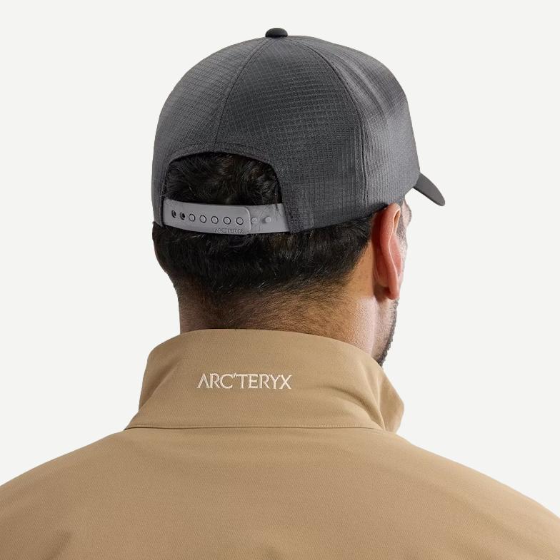 Black and cloud-colored Arcteryx Bird Word Trucker Hat shown from the back view, featuring a mesh trucker style and embroidered logo.