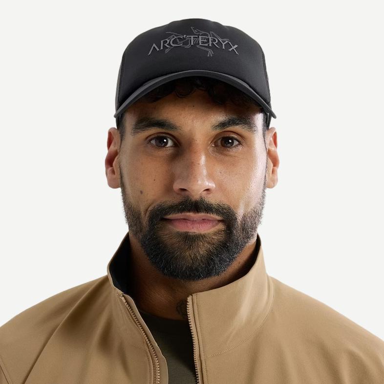 Black and cloud-colored Bird Word Trucker Hat by Arcteryx with front view, mesh back, and adjustable snap closure.