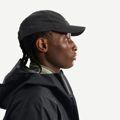 Black Bird Word Cap by Arc’teryx, a stylish black hat featuring the brand logo, shown from a side view.