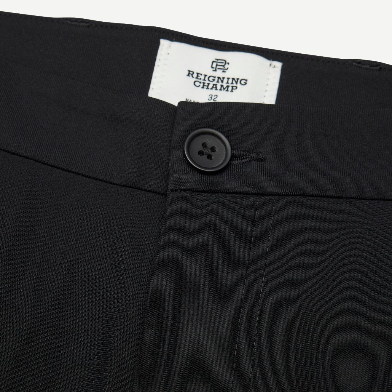 Reigning Champ black stretch warp knit coach's slim pants displayed on a hanger with a close-up view of fabric texture.