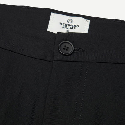 Reigning Champ black stretch warp knit coach's slim pants displayed on a hanger with a close-up view of fabric texture.