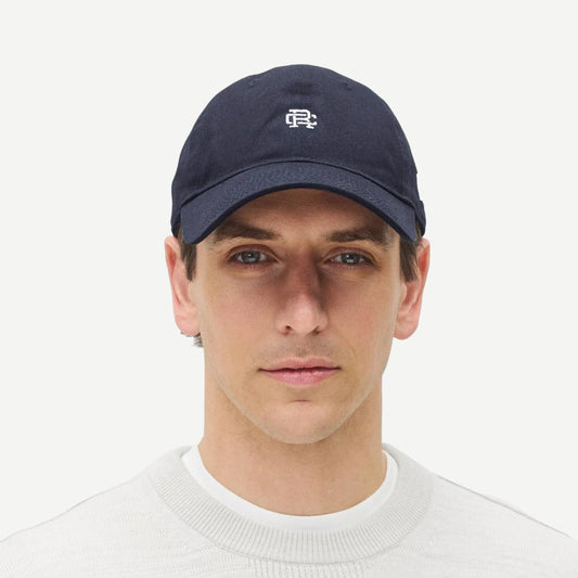 Reigning Champ navy New Era 9Twenty Mini Monogram cap with adjustable strap, front logo, and curved brim.